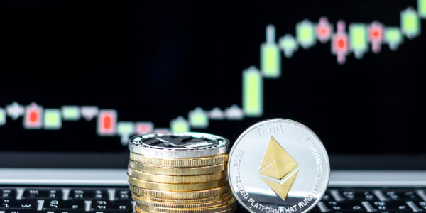 A close-up of stacked coins with a prominent silver Ethereum (ETH) token in focus, placed in front of a glowing candlestick chart showing market volatility and potential recovery trends.