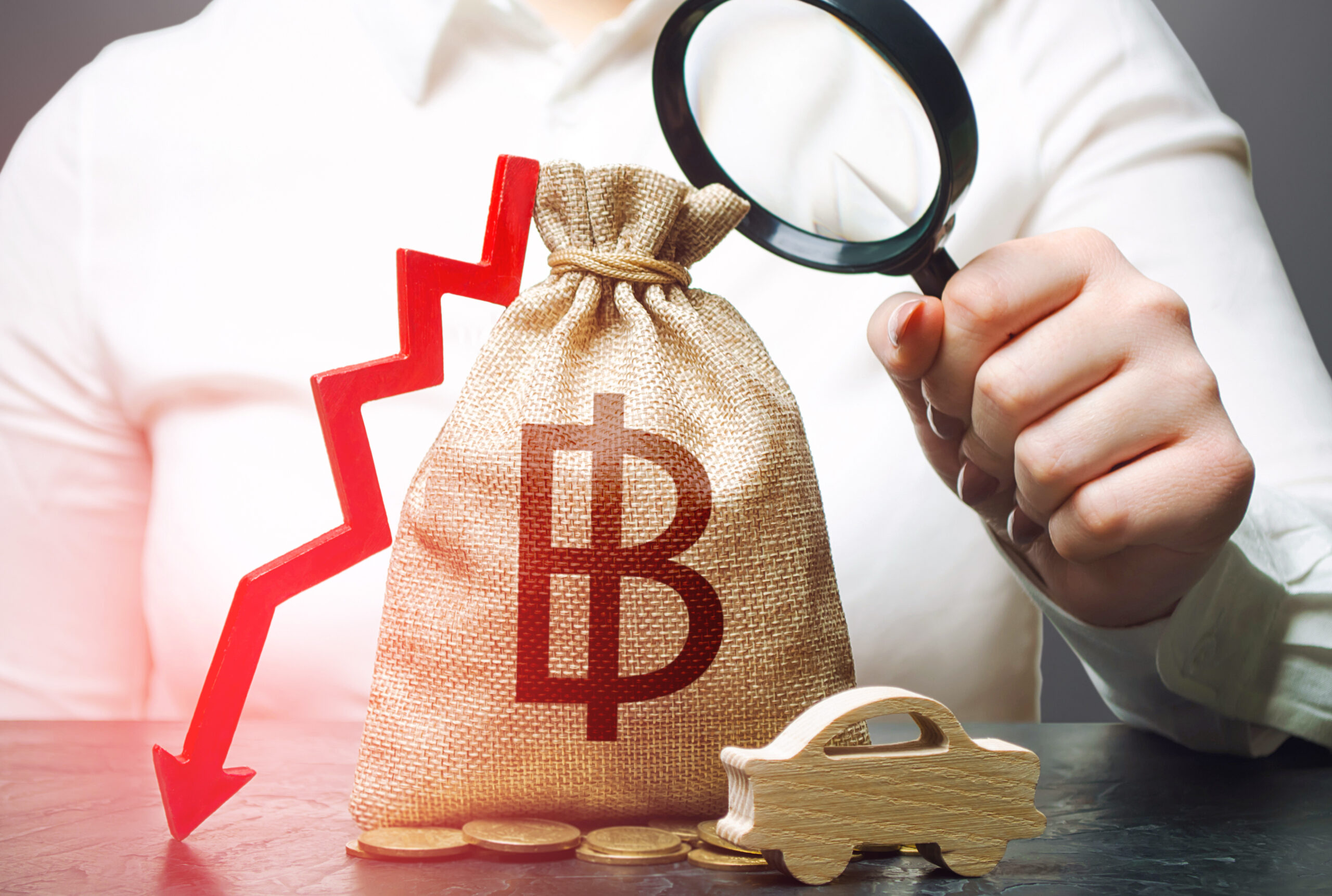 Woman holding a money bag with a Bitcoin symbol and a red downward arrow, symbolizing financial uncertainty and market decline.