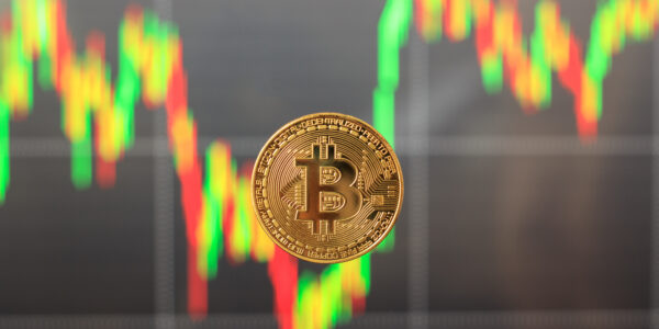 Single Bitcoin in focus with a blurred, falling candlestick chart in the background, symbolizing market panic and asset sell-offs.