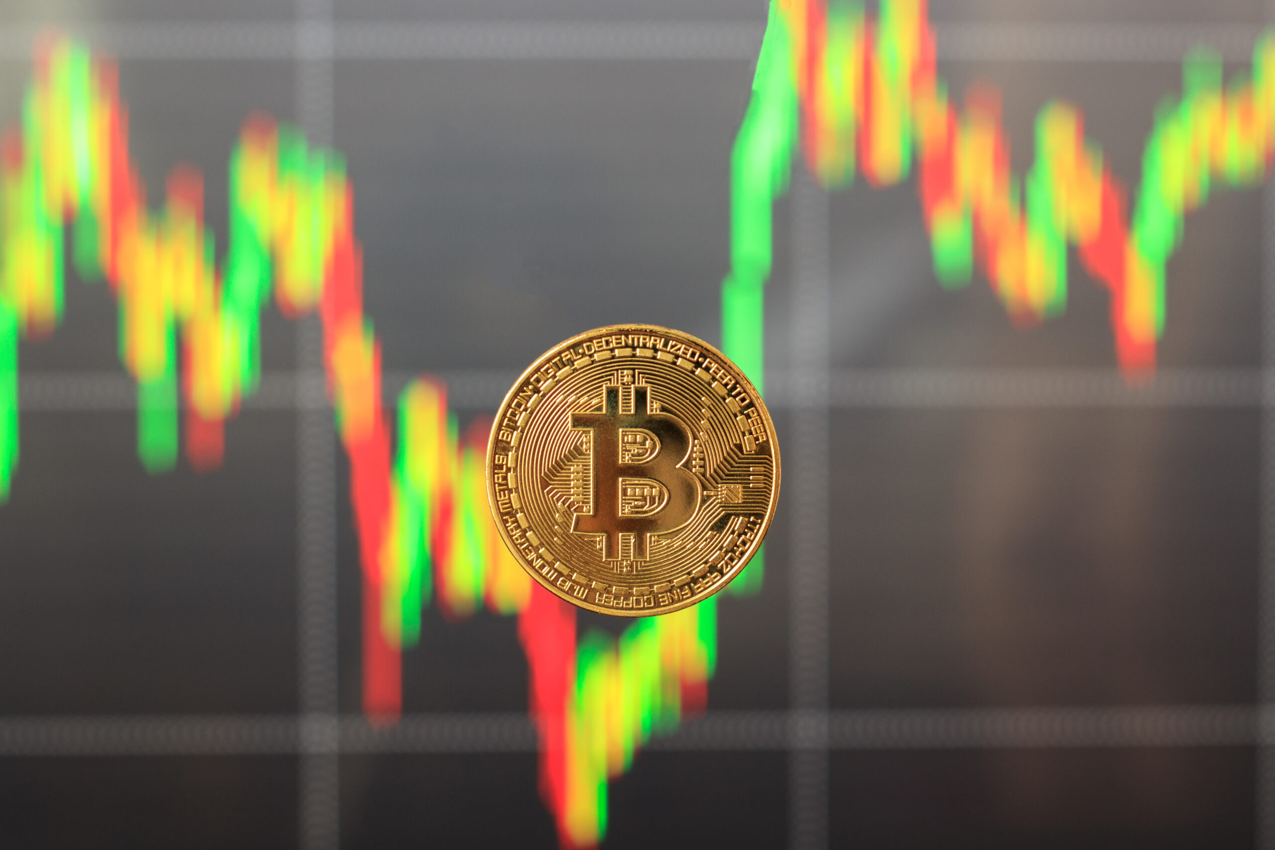 Single Bitcoin in focus with a blurred, falling candlestick chart in the background, symbolizing market panic and asset sell-offs.