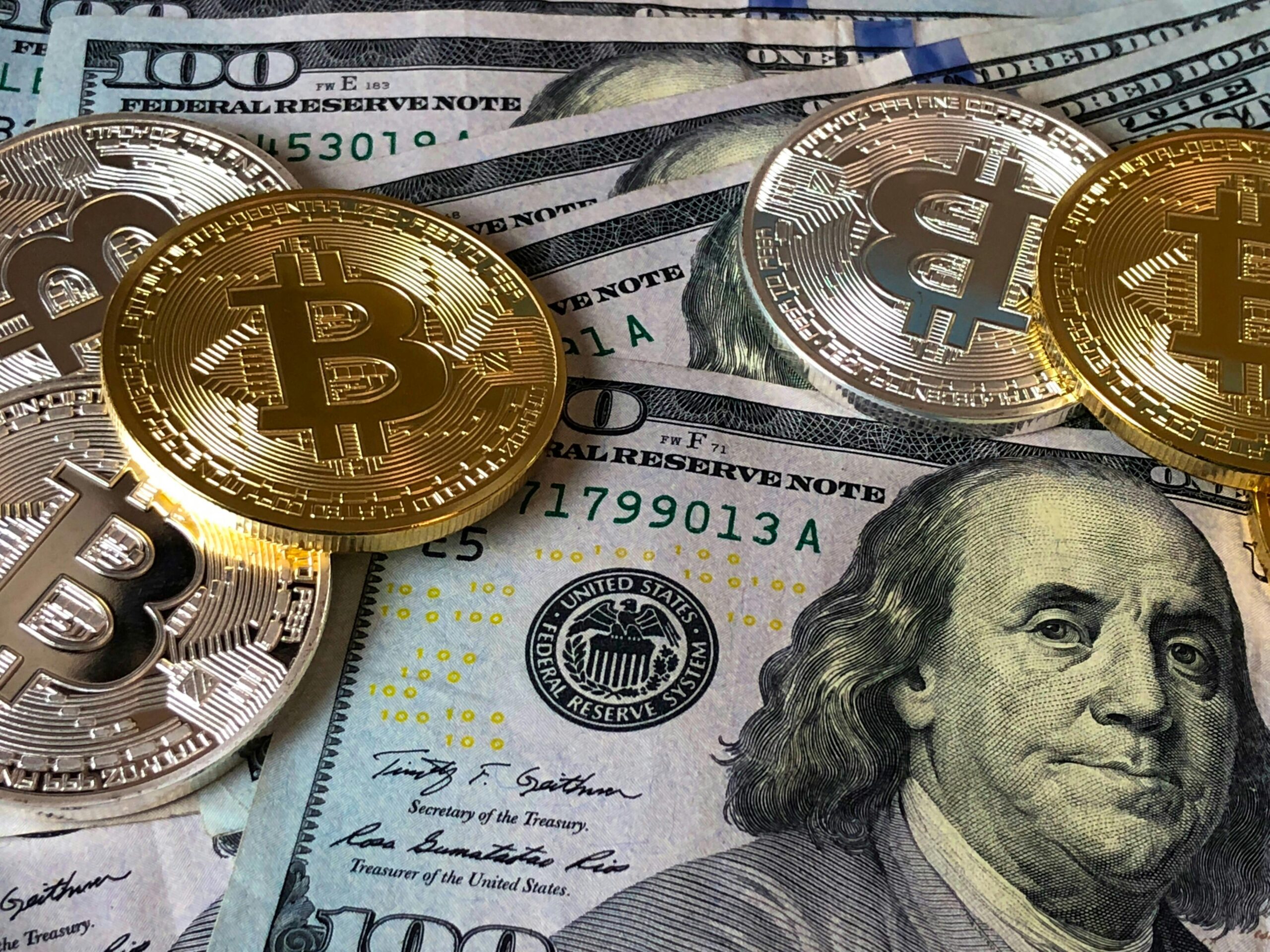 A close-up of gold Bitcoin coins placed on top of U.S. dollar bills, symbolizing the financial growth of Bitcoin startups amid a cooling crypto market.