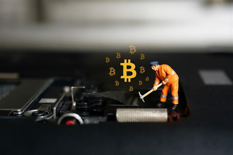Miniature figure placing a glowing Bitcoin on a computer motherboard, representing Arizona’s growing support for digital mining rights.